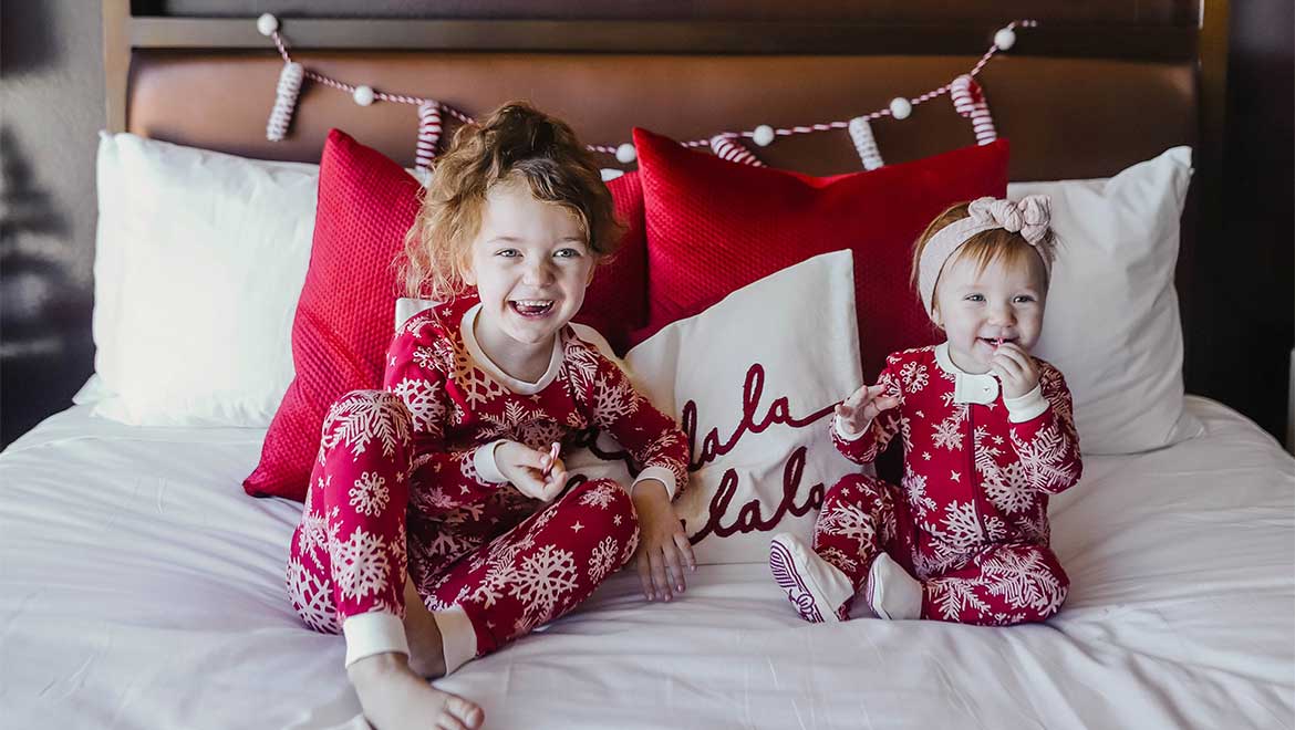 Two little girls sitting on a bed in their Christmas pjs